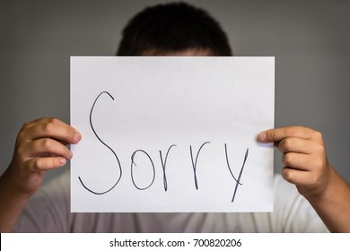 A Boy Holding Up A Paper Saying Sorry