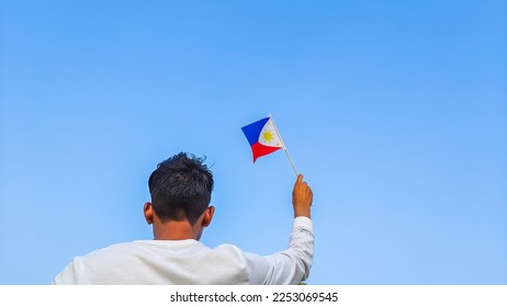 Boy holding Philippines flag against clear blue sky. Man hand waving Filipino flag view from back, copy space for text - Powered by Shutterstock