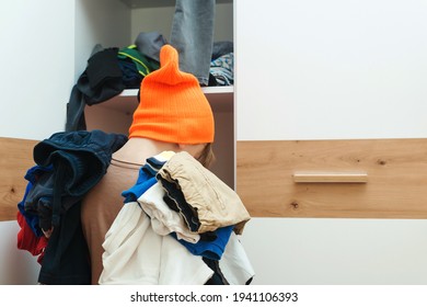 Boy Holding Pile Of Dirty Clothes. Untidy Clutter Clothing Closet. Messy Home Kid's Room. Home Chores Housework. Mess In The Wardrobe. Many Scattered Clothes In Children Bedroom.