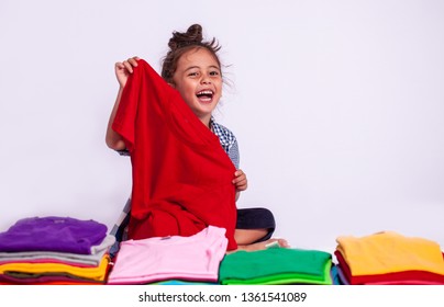 A Boy Holding Red Tee Shirt Behind Colorful Pile Of Tee Shirts In Tee Shirt Shop On White Background