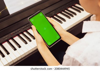 Boy holding the smartphone with green screen near the electronic piano. Mockup for mobile music apps. Piano lesson online. Online music education - Powered by Shutterstock