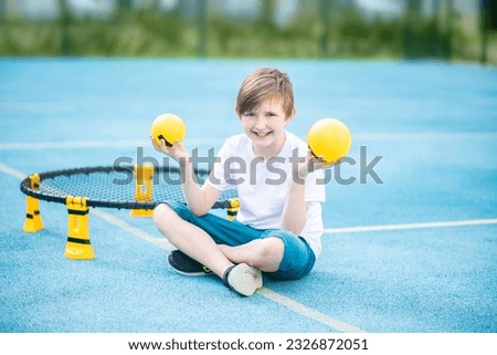 boy holding a yellow ball for a sport game spikeball. the child will sit in front of the "trampoline" for the spike ball, in a miniature analogue of volleyball