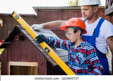 The boy holds the building level, checking the accuracy of the dog house roof.