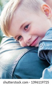 The Boy Hugged His Father And Put His Head On His Shoulder. A Child Is Seven Years Old, He Is Blond. The Father Is Wearing A Black Jacket.