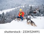 Boy with husky dog sledding on winter mountain, enjoying a sledge ride in a beautiful snowy winter park. Winter fun kids activities.