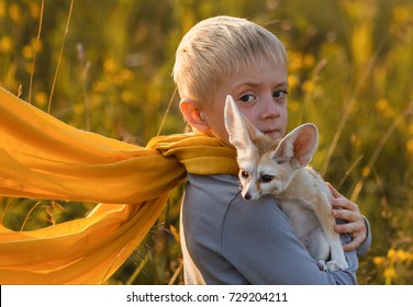 A boy in the image of the Little Prince Antoine Exupery holds a fox in his hands. Fennec tame. A child in a yellow scarf  look at the camera. Fox. Fennecus zerda. Le Petit Prince