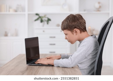 Boy with incorrect posture using laptop at wooden desk indoors
