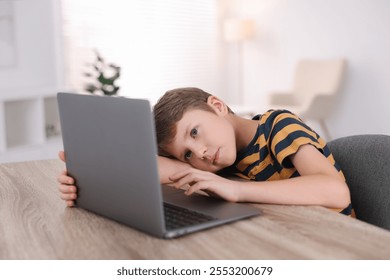 Boy with incorrect posture using laptop at wooden desk indoors