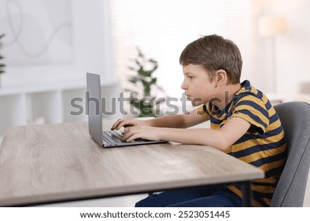Boy with incorrect posture using laptop at wooden desk indoors