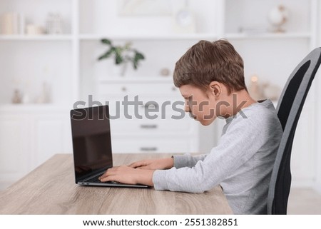 Boy with incorrect posture using laptop at wooden desk indoors