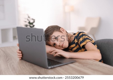 Boy with incorrect posture using laptop at wooden desk indoors