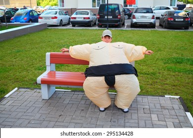 Boy In Inflatable Sumo Wrestler Suit Sitting On Bench On Territory Near House
