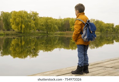 Boy in jacket with backpack standing at the pier