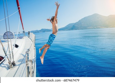 Boy Jump In Sea Of Sailing Yacht On Summer Cruise. Travel Adventure, Yachting With Child On Family Vacation.