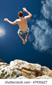 Boy Jumping Off Cliff Into Blue Water