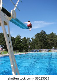 Boy Jumping Off The High Diving Board At A Public Swimming Pool.