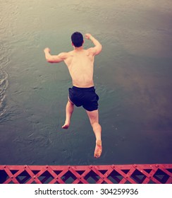 a boy jumping off an old train trestle bridge into a river toned during summer time toned with a retro vintage instagram filter effect with a motion blur 