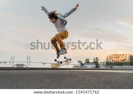 Boy jumping on skateboard at the street. Funny kid skater practicing ollie on skateboard at sunset.
