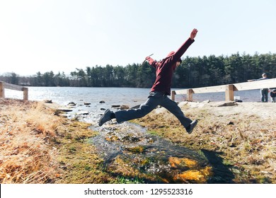 Boy Jumping Over A Stream. Agile Child Outside