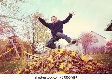 Boy Jumping In A Pile Of Autumn Leaves