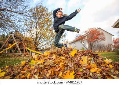 Boy Jumping In A Pile Of Autumn Leaves. Focus On Top Of Leaves, 