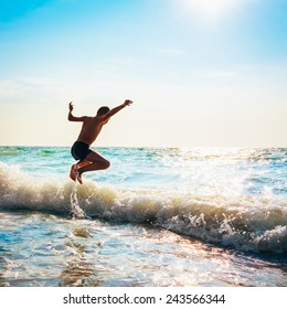 Boy Jumping In Sea Waves. Jump Accompanied By Water Splashes. Summer Sunny Day, Ocean Coast