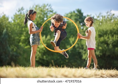 Boy jumps through hula hoop while two girls are holding it