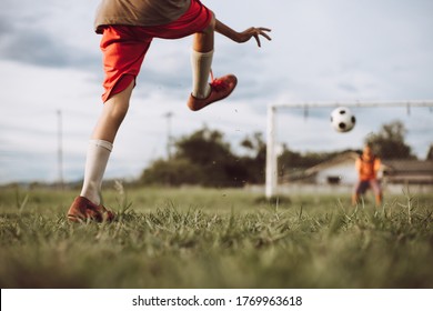 Boy Kicking A Ball While Playing Street Soccer Football On The Green Grass Field For Exercise. Outdoor Sport Activity For Children And Kids Concept Photo.