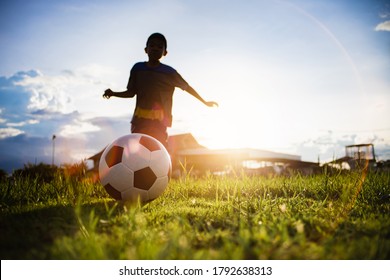 Boy kicking a ball while playing street soccer football on the green grass field for exercise. Outdoor sport activity for children and kids concept photo with copy space.