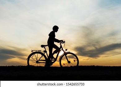 Boy , Kid 10 Years Old Riding Bike In Countryside, Silhouette Of Riding Person At Sunset In Nature