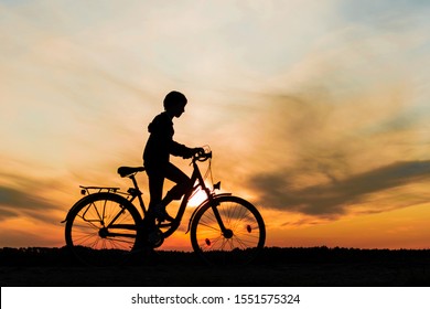 Boy , Kid 10 Years Old Riding Bike In Countryside, Silhouette Of Riding Person At Sunset In Nature