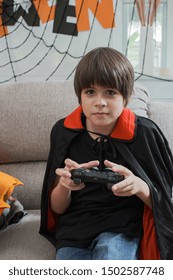 Boy Kids Smiling And Dress Up As Halloween Vampire Costume Holding Joystick To Play Halloween Game In Living Room At Home