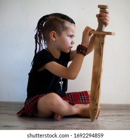 A Boy In A Kilt Sits With A Sword, Looks Forward.