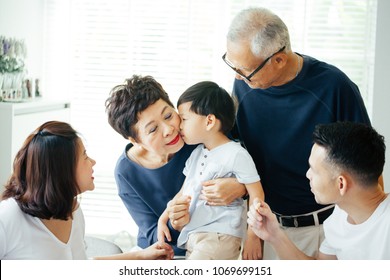 Boy Kissing Grandmother On Cheeks With The Whole Asian Family Of Three Generations Together At Home