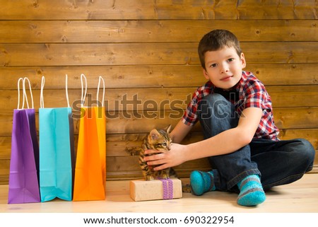 Boy with kitten, next to shopping bags with shopping and gift, on the floor against a wooden wall