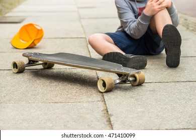 Boy With Knee Injury Sitting Near Skateboard On Sidewalk