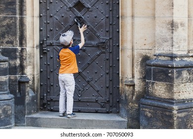 Boy knocking in door knocker on old medieval castle. Textured stone walls. kid begging for entrance to the house