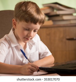 boy with laptop at the table taking notes with a pen on a sheet of paper