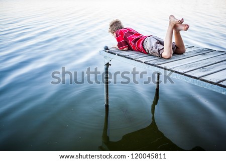 Boy laying on a dock by a lake