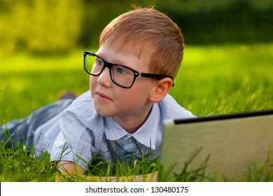 Boy Laying On Green Grass In The Park With Laptop, Looking To The Right Side