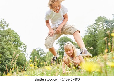 Boy in leapfrog with his sister on a meadow in summer