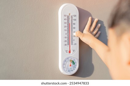 The boy learn to checking the numbers on a thermometer on a gray wall outside the house with copy space. Temperature checking concept.