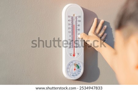 The boy learn to checking the numbers on a thermometer on a gray wall outside the house with copy space. Temperature checking concept.