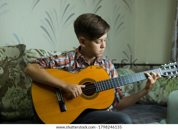 Boy learn to play guitar online. A boy with a\
guitar sits in front of a laptop. Acoustic guitar, the hands of a\
young musician play the\
guitar.