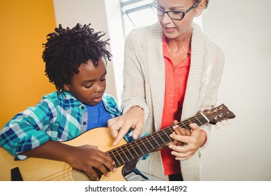 Boy learning how to play the guitar with the help of a teacher