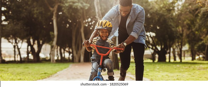 Boy learning to ride a bicycle with his father in park. Father teaching his son cycling at park. - Shutterstock ID 1820525069
