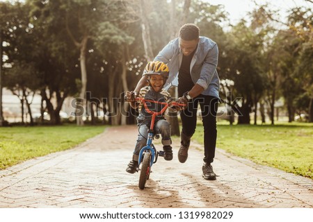 Boy learning to ride a bicycle with his father in park. Father teaching his son cycling at park.