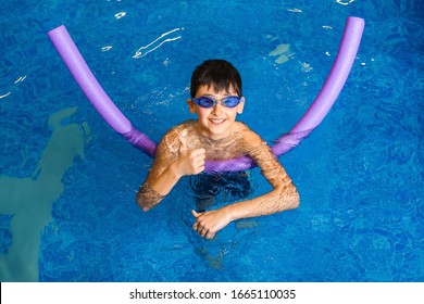 The Boy Learning Swimming In The Pool Using A Foam Stick And Goggles. Top View.