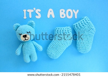 It's a boy lettering, crochet bear and baby booties on blue background. Baby boy birth, new life, family concept. Greeting card idea for newborn. Pregnancy announcement. Flatlay, top view