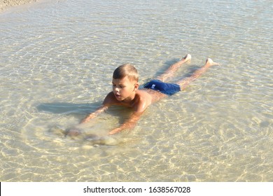 Boy Lie In Puddle On Summer. Child On Beach. Boy Lay In Dirty Water.  Happy Carefree Childhood.  Joyful Child In Muddy Puddle On Sand. Life In Village During Summer. Childhood Without Phone